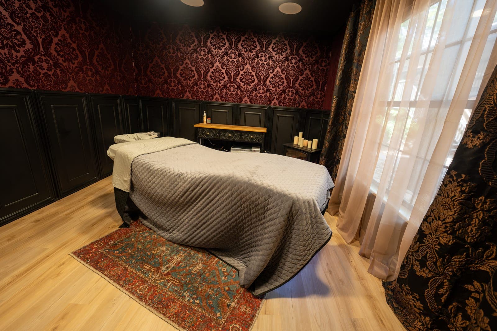Treatment room with a damask wall, dark wainscot and sheer curtains at the window